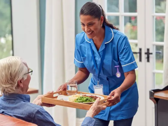 Home 8 Care worker serving a freshly prepared meal to a senior resident as part of elderly nutrition support